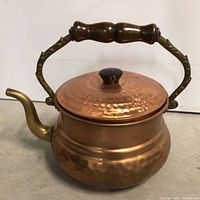 Front view of hammered copper kettle with lid, wooden handle, brass spout