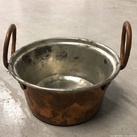Angled view of copper saucepan showing exterior and one handle
