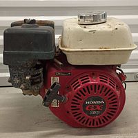 Front view showing red recoil housing with Honda GX marking, fuel tank, air cleaner, muffler