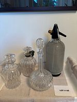 All four items grouped: two ribbed decanters, cut glass decanter, wire-mesh seltzer bottle