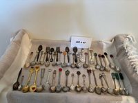 Overview of all souvenir teaspoons and forks laid out on fabric