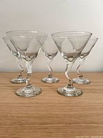 Five clear glass martini glasses with twisted stems arranged on wood surface