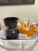 Two shiny black bowls stacked, orange bowl with utensils, black salad servers in foreground