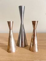 Front view of three metal candle holders showing sizes, shapes and finishes