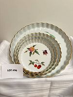 Stacked view of all four scalloped dishes showing fruit motifs and gold rims