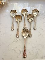 Six matching ornate berry spoons displayed on marble surface