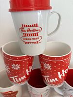 Plastic travel cup atop three red sweater mugs
