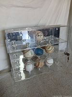 front view of acrylic display case showing mirrored back, three shelves, pedestals, key lock and seven baseballs