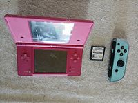 Pink Nintendo DS handheld console, Nintendo DS game cartridge, neon blue Joy-Con laid out on surface