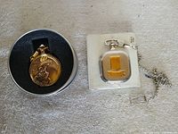 Two pocket watches: gold-tone in tin, silver-tone in box with chain