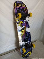 Full view of Tony Hawk skateboard leaning, showing graphic, trucks, wheels