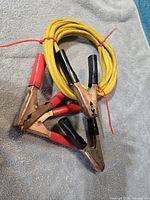 Coiled yellow jumper cable with four copper alligator clamps, red and black grips visible