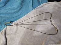 Full view of wire carpet beater showing heart-shaped head and green wooden handle