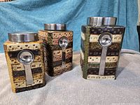 Front view of the three differently sized ceramic canisters with stainless lids and attached measuring scoops