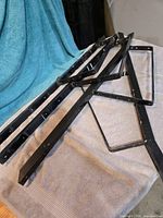 Four black metal bench frames laid out on towel showing overall shape and mounting holes