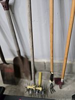 Group of four long-handled garden tools leaning against wall
