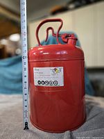 Full view of red metal safety can with tape measure indicating 18 in height