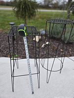 Square and round black metal plant stands, tape showing 27-inch height on square stand