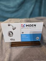 Sealed retail box showing Moen Adler 82603SRN tub and shower set image and branding