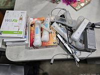 Pile showing Wii console accessories, multiple controllers, power supply, sensor bar, cables and stack of Wii game cases