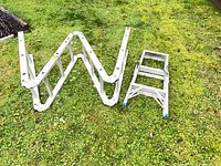 Articulating ladder folded in Z-shape beside step ladder on grass