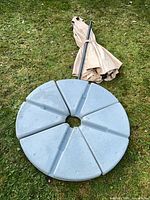 Umbrella pole and folded canopy beside six-segment base on grass