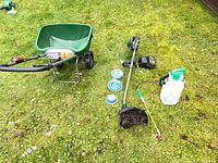 Entire lot showing trimmer, spreader, sprayer, batteries, charger and spools on grass