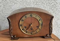 Front view of wooden mantel clock showing dial, missing glass bezel, carved side scrolls