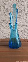 Front view of tall blue swung glass vase on wooden surface