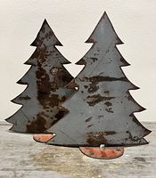 Two steel evergreen tree sculptures side by side showing size and patina