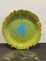 Front view of large round green, orange and blue fused glass platter on stand