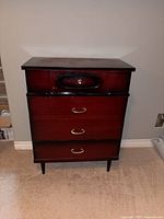 Full front view of reddish mahogany four-drawer dresser with black trim and tapered legs