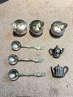 Overview of 3 tea tins, 3 spoons, 2 miniature teapots on carpet