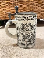 Side view of porcelain stein showing tavern scene and German script, attached pewter lid and handle