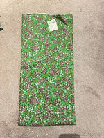 Full view of folded green floral cotton fabric on carpeted floor