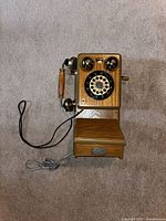 Front view of wall-mounted rotary telephone with handset, cords visible