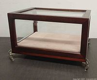 Front angled view of the glass and wood display case showing metal feet