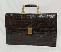 Front view of brown crocodile-embossed leather briefcase with gold-tone handle and lock