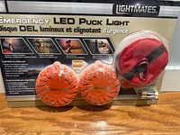 Front of sealed retail package showing two orange puck lights and red pouch