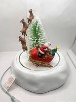 Front view of animated sleigh figurine showing Santa, reindeer, tree and base with power cord