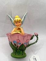 Front view of Tinker Bell figurine in pink flower cup with tag visible