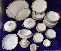 Full set of stacked plates, bowls, platters, covered bowls, gravy boat, creamer and sugar bowl displayed on dark cloth