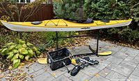 Side view of yellow Eddyline Rio kayak on Sparehand stand with crate of accessories including paddle, roof racks, ropes, straps