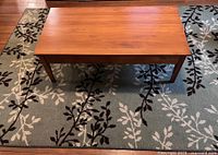 Top view of maple coffee table centered on sage leafy rug