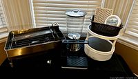 All five kitchen items grouped: dish rack, beverage dispenser on stand with drip tray, white 2-tier turntable, black organizer basket, metal utensil tray