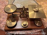 Top view of brass postal scale on wooden base with three weights