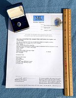 Ring, appraisal document, and box displayed with ruler for scale