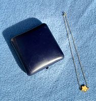 Closed blue jewellery box beside gold necklace showing overall length