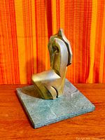 Full view of bronze sculpture on green marble base, wooden surface and striped fabric backdrop