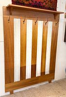 Full view of teak coat rack showing hooks, shelf, upholstered panels